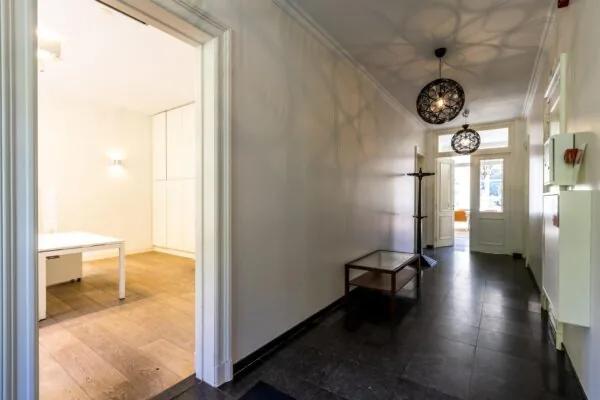 Lichte hal met zwarte vloertegels, moderne hanglampen en zicht op een kantoorruimte en buitendeur aan de Langbroekerdijk A.